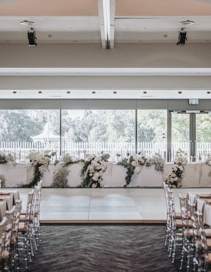 Long Bridal table draped in white roses behind a dance floor and two long guest tables.